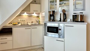 Una cocina moderna con armarios blancos, horno empotrado, microondas y cafetera. Dos cuadros enmarcados están sobre la encimera.