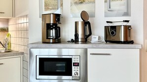 Una cocina moderna con microondas integrado, cafetera y tostadora. Tres cuadros enmarcados decoran la pared sobre la encimera.