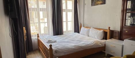 A bedroom with a bed, bedside table, chair, and a desk with a remote control.