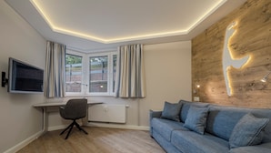 Quarto moderno com parede em madeira, um sofá azul, uma escrivaninha com cadeira e uma TV fixada na parede.