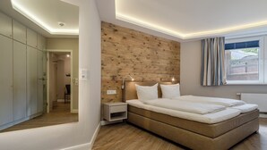 Quarto moderno com cabeceira de madeira, uma cama grande, luminárias de cabeceira e vista para o exterior pela janela.