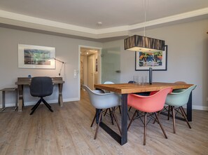 A dining area with a wooden table and colorful chairs, a desk with a lamp, and framed artwork on the walls. - Modern vacation apartment with 3 rooms on approx. 87 m², for max. 4 persons (Westerland)