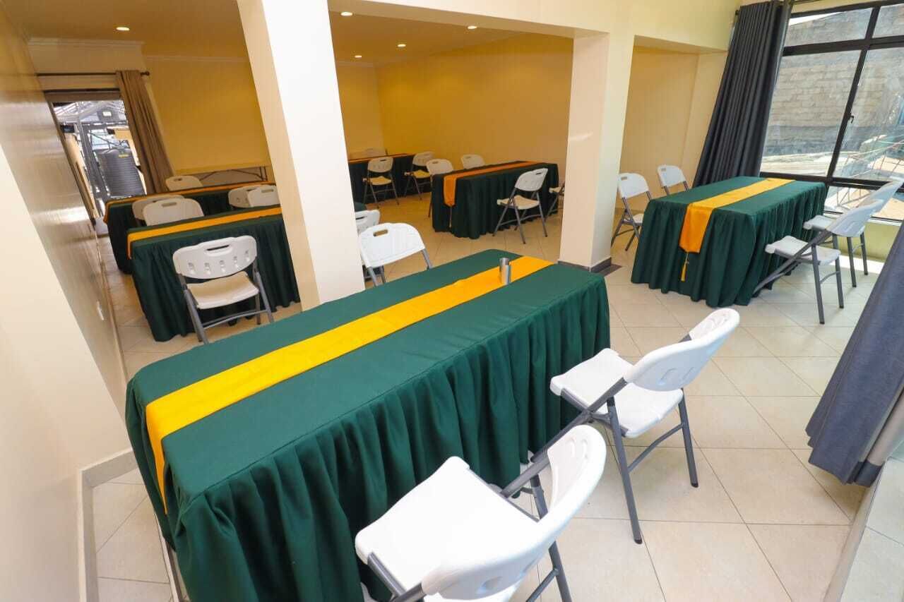 A conference room with tables covered in green tablecloths with yellow stripes, white chairs, and a large window providing a view of the outside.