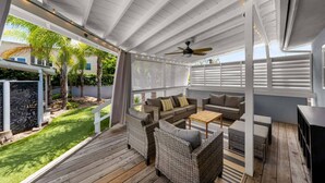 Eine überdachte Terrasse im Freien mit Korbmöbeln, einem Deckenventilator und Blick auf einen gepflegten Garten.