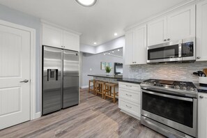 A modern kitchen with white cabinetry, stainless steel appliances, and a wooden floor.