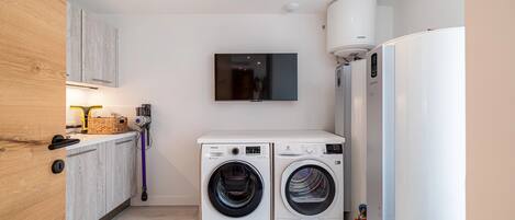 A compact laundry room with two front-loading washing machines, a wall-mounted television, and a built-in refrigerator.