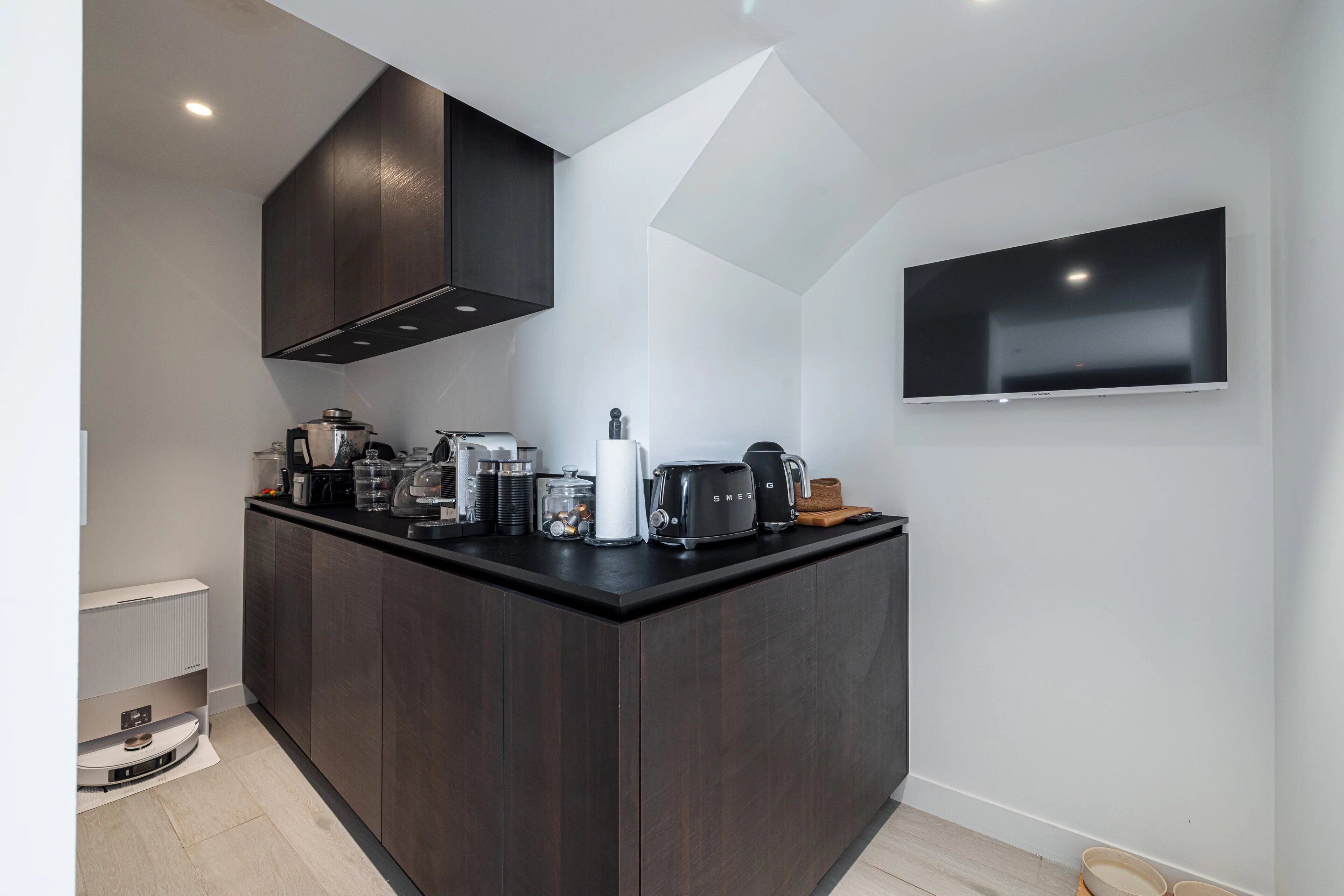 Une cuisine moderne avec des meubles de couleur sombre, un îlot central et un téléviseur à écran plat fixé au mur.