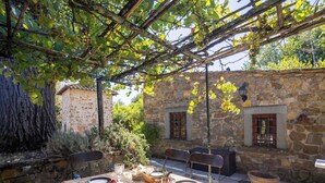 An outdoor dining area with a stone wall, a pergola with vines, and a rustic table set for two.