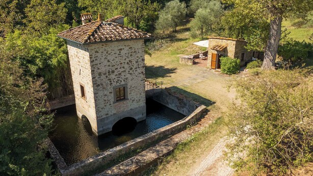 A stone tower with a small window, a water well, and a stone pathway leading to a rustic building.