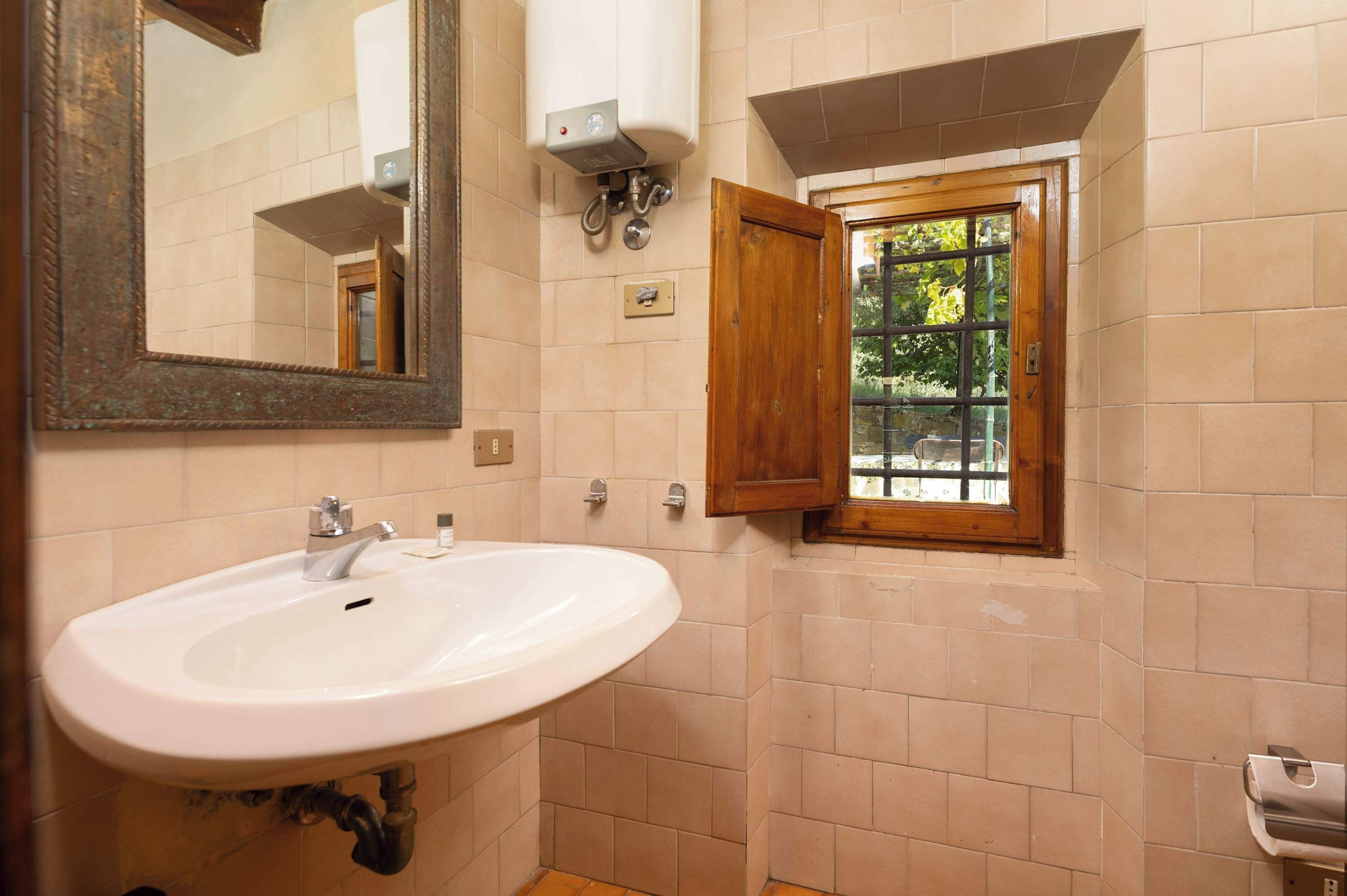 A bathroom with a white sink, a mirror, a window with a wooden frame, and a towel dispenser.