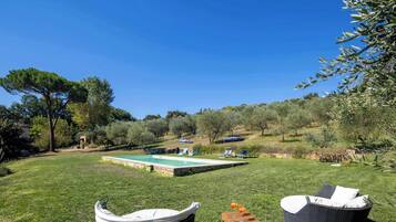 Zona de piscina con dos sillones de mimbre, una mesa pequeña con bebidas y un bote cubierto.