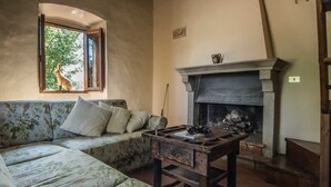 A cozy living room with a sofa, a fireplace, and a window with a view of greenery.