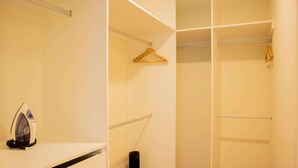 Ein begehbarer Kleiderschrank mit Kleiderstange, einem Bügelbrett und einem schwarzen zylindrischen Gegenstand.