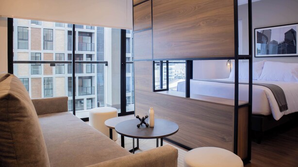 Ein modernes Hotelzimmer mit großem Fenster, einem Bett, einer Couch und einem kleinen Tisch.