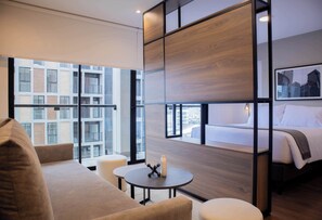 Habitación de hotel moderna con un gran ventanal, una cama, un sofá y una pequeña mesa.