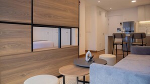 Ein modernes Hotelzimmer mit einer Wand in Holzoptik, einem runden Tisch mit Stuhl, einer Couch und einer Küchenzeile.