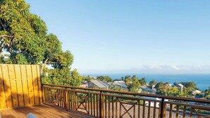 Terraza de madera con asientos blancos acolchados y una mesa, con vistas a la costa.