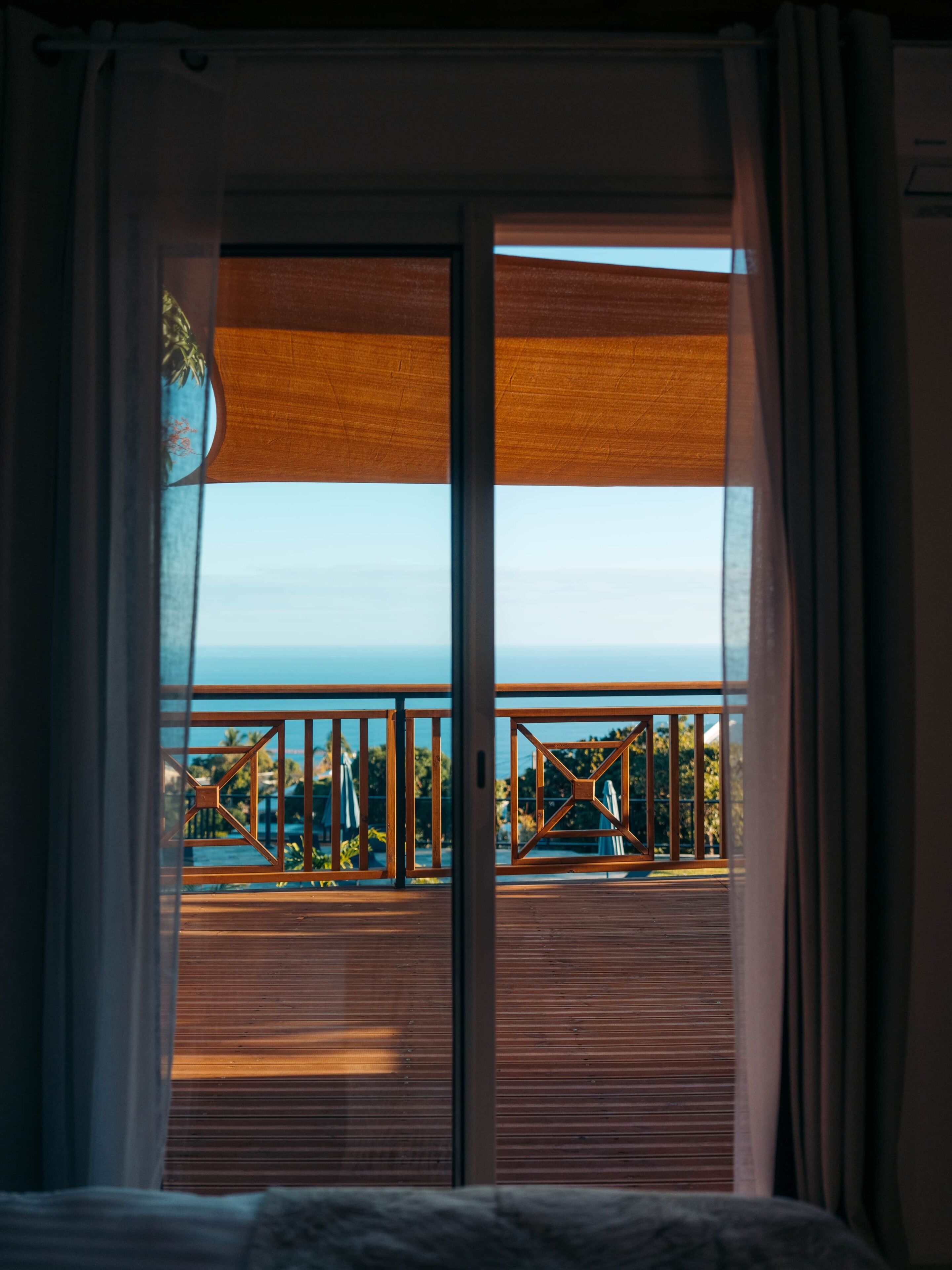 A room with a large sliding glass door leading to an outdoor deck with a view of the ocean and a pool.