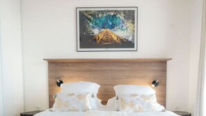 Una cama bien hecha con colcha de motivos florales, cabecera de madera y un cuadro enmarcado encima.