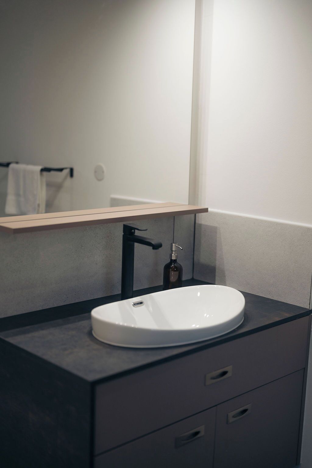 Un baño moderno con un lavamanos blanco, encimera oscura y un espejo encima.