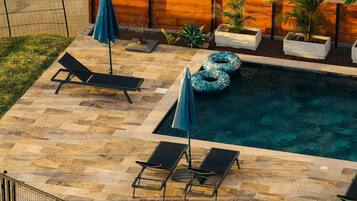 Une piscine extérieure entourée d’une clôture en bois et agrémentée de plantes en pot, avec des chaises longues et des parasols à proximité.