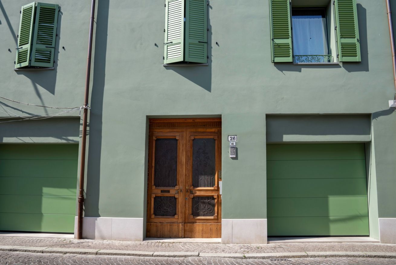 Un edificio con fachada verde, una puerta doble de madera y dos puertas de garaje verdes.