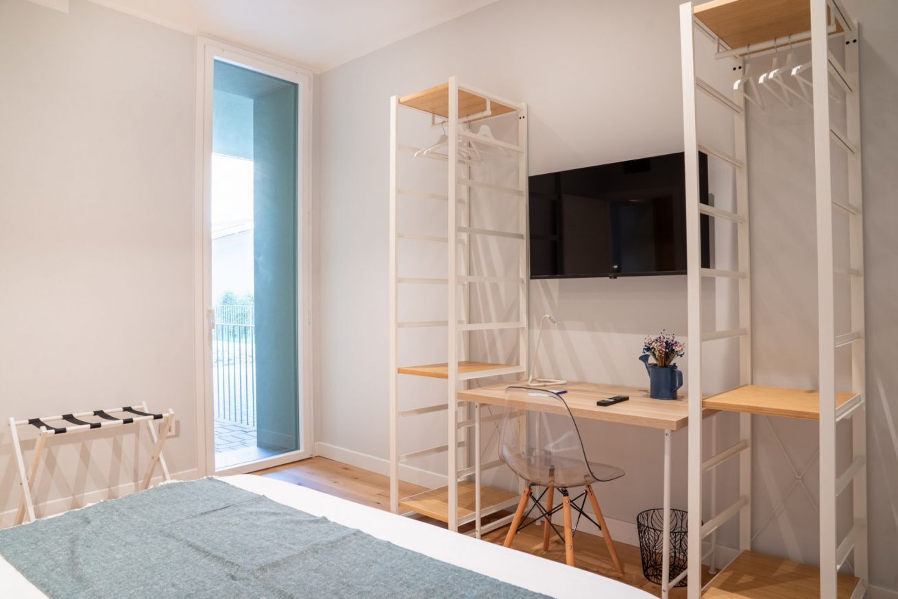 Un dormitorio con cama, escritorio, silla, televisor y armario.
