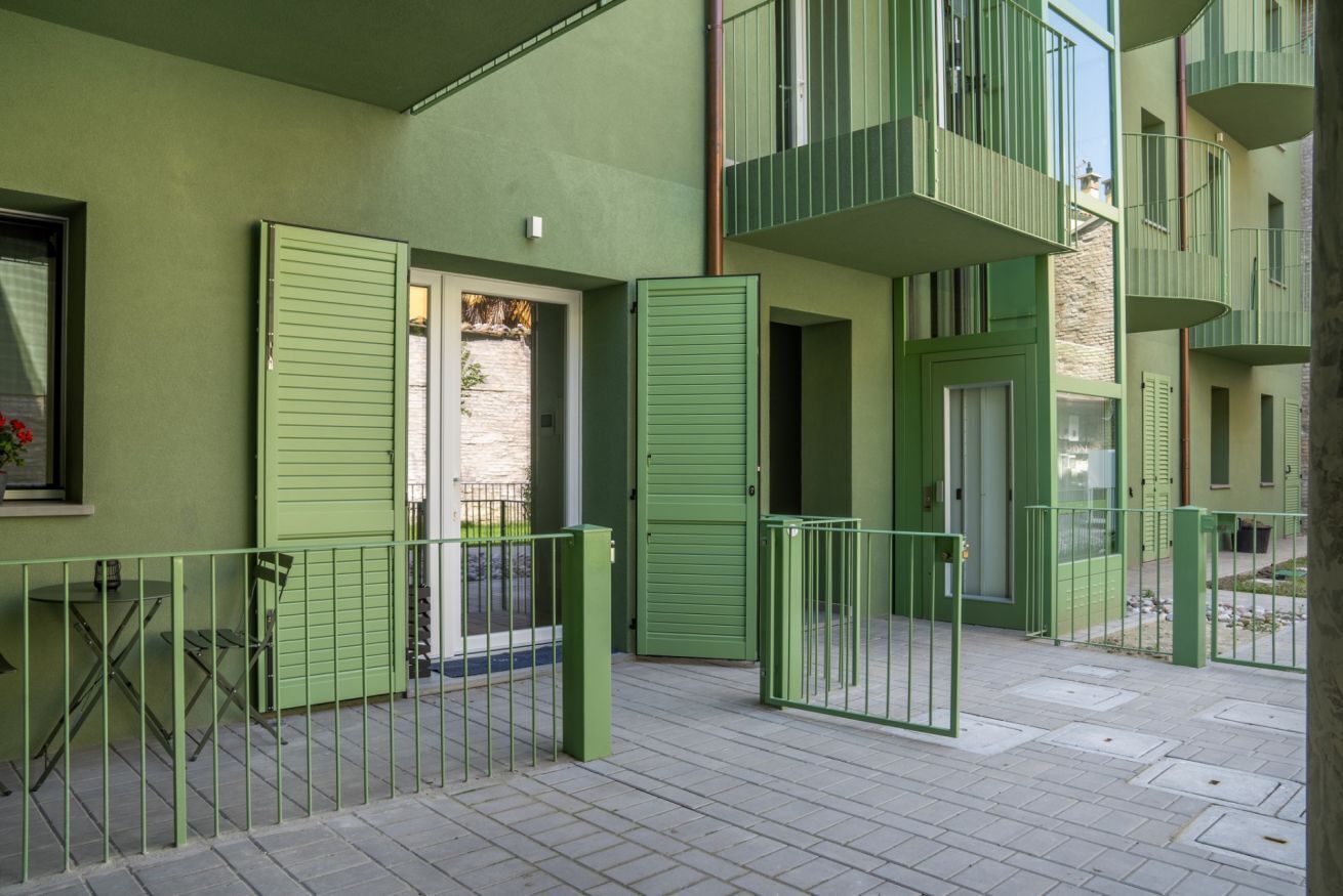 A green exterior of a building with balconies, a door, and a small table with chairs.