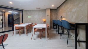 A modern dining area with a white table and chairs, a staircase, and a wall-mounted lamp. - Maharlika City Inn  (Bacolod)