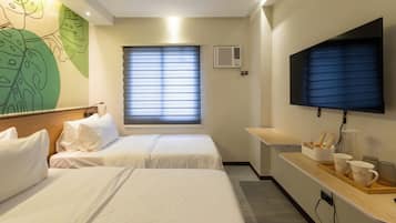 A hotel room with two beds, a flat-screen TV, a window with blinds, and a wall-mounted air conditioner.