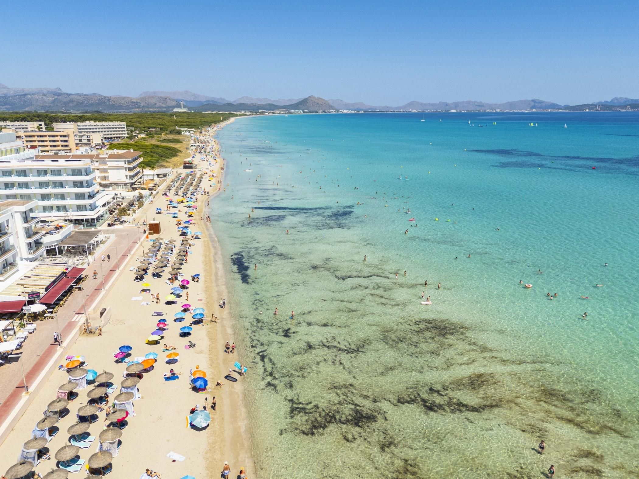 Ein Küstenstrand mit klarem Wasser, Sonnenschirmen und Badegästen.