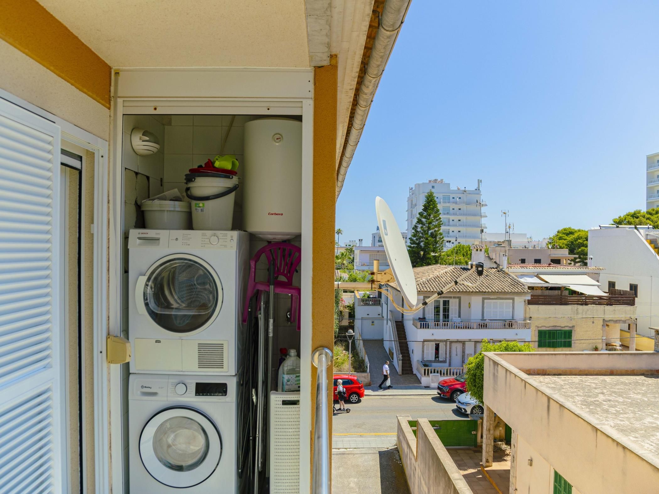 A balcony with stacked laundry appliances, a satellite dish, and a view of a residential street.