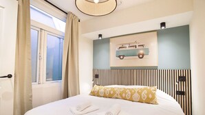 A neatly made bed with two towels, a patterned pillow, and a wall-mounted picture of a vintage car. - Modern apartment near Scheveningen beach (Den Haag)