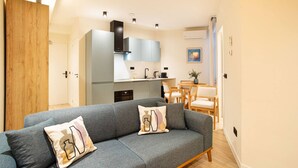 A modern living room with a grey sofa, wooden door, and a kitchen area with a dining table and chairs. - Modern apartment near Scheveningen beach (Den Haag)