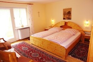 Une chambre à coucher avec un lit en bois, deux tables de chevet, une commode, un radiateur, une chaise et une fenêtre avec des rideaux.