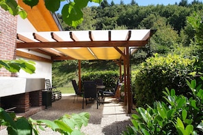 Un patio couvert avec des meubles d’extérieur, un mur en briques et un jardin.