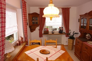 Une salle à manger avec une table en bois, des chaises, un lustre et une fenêtre avec des rideaux.