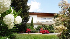 Un bâtiment à l’extérieur blanc, doté d’un balcon et d’un jardin bien entretenu où poussent diverses plantes et fleurs.