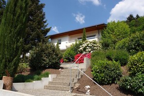 A modern house with a staircase leading to a balcony, surrounded by lush greenery and flowering plants. - Apartment 'Schwarzwaldsuite - Apt 1' with Shared Terrace, Shared Garden and Wi-Fi (Seelbach)