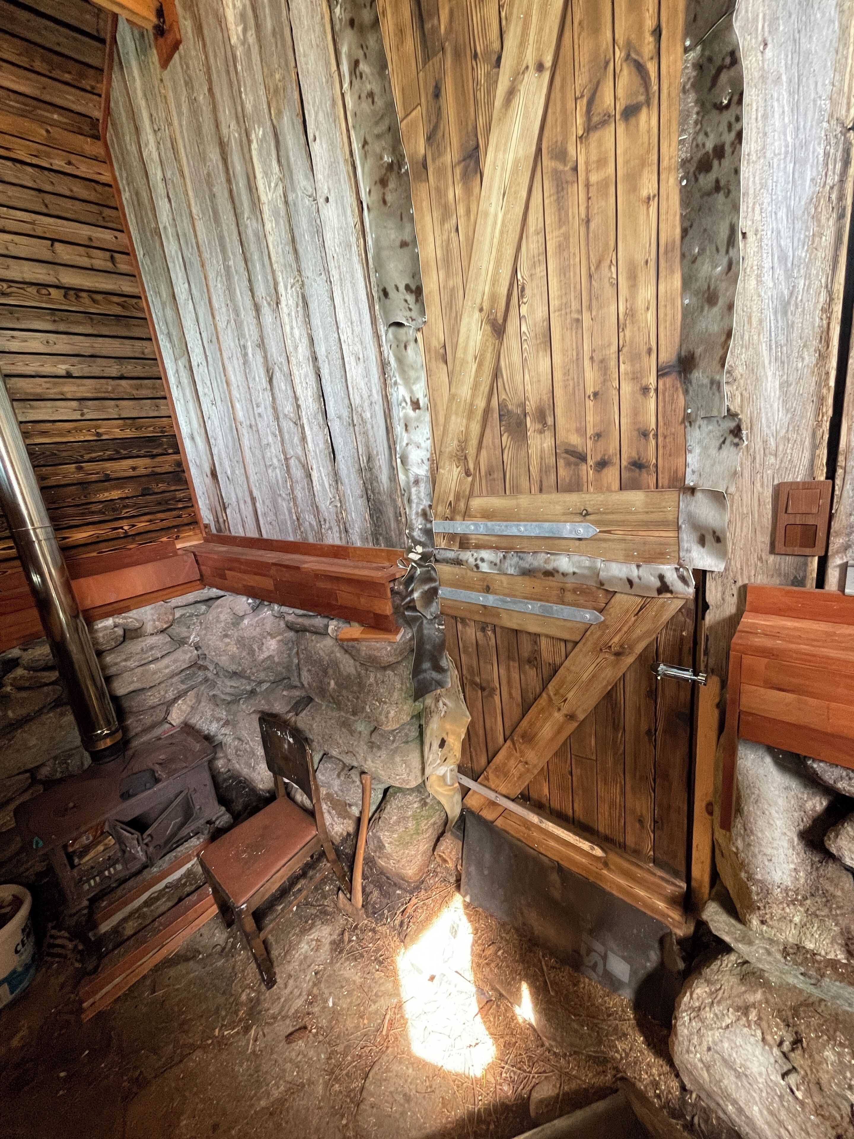 A rustic interior with stone walls, wooden beams, and a large wooden door.