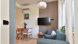 Una sala moderna con un televisor de pantalla plana montado en una pared de listones, un comedor con una mesa y sillas de madera, y una zona de estar acogedora con un sofá.