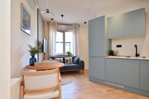 A modern kitchen with blue cabinets, a wooden dining table, and a blue sofa.