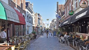 Una calle adoquinada bordeada de cafés y restaurantes, con mesas al aire libre y diversos estilos arquitectónicos.