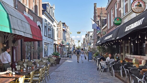 Una calle adoquinada bordeada de cafés y restaurantes, con mesas al aire libre y diversos estilos arquitectónicos.