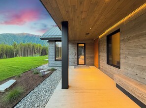 A modern building with a wooden exterior, a concrete pathway, and a view of a green landscape with trees and mountains in the background.