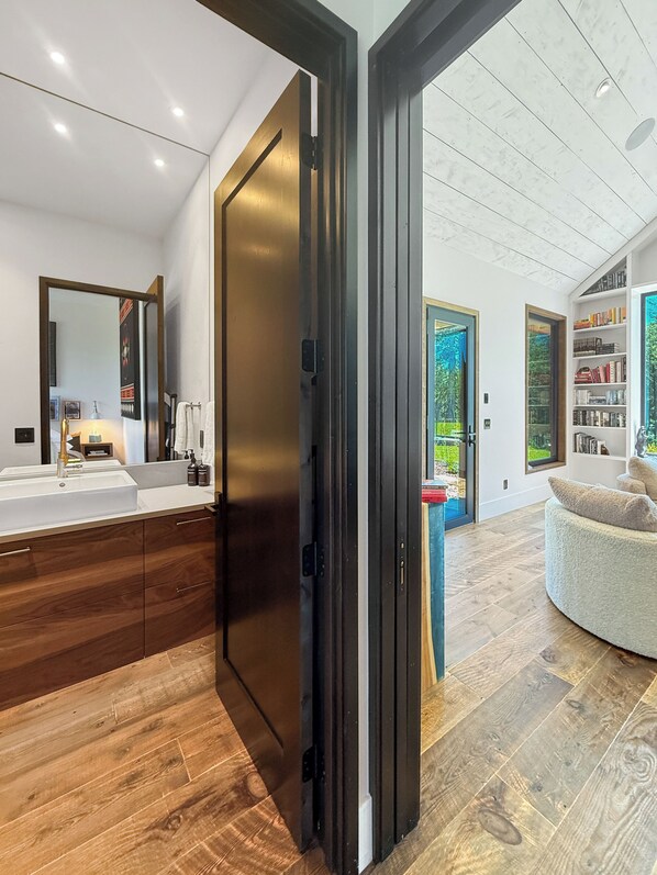 A modern bathroom with a large mirror, wooden cabinets, and a white sink.
