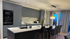 A modern kitchen with grey cabinets, a white countertop, and a central island with bar stools.