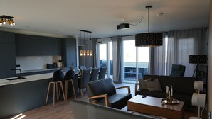 A modern kitchen with dark cabinetry, a dining area with black chairs, and a living space with a sofa and coffee table.