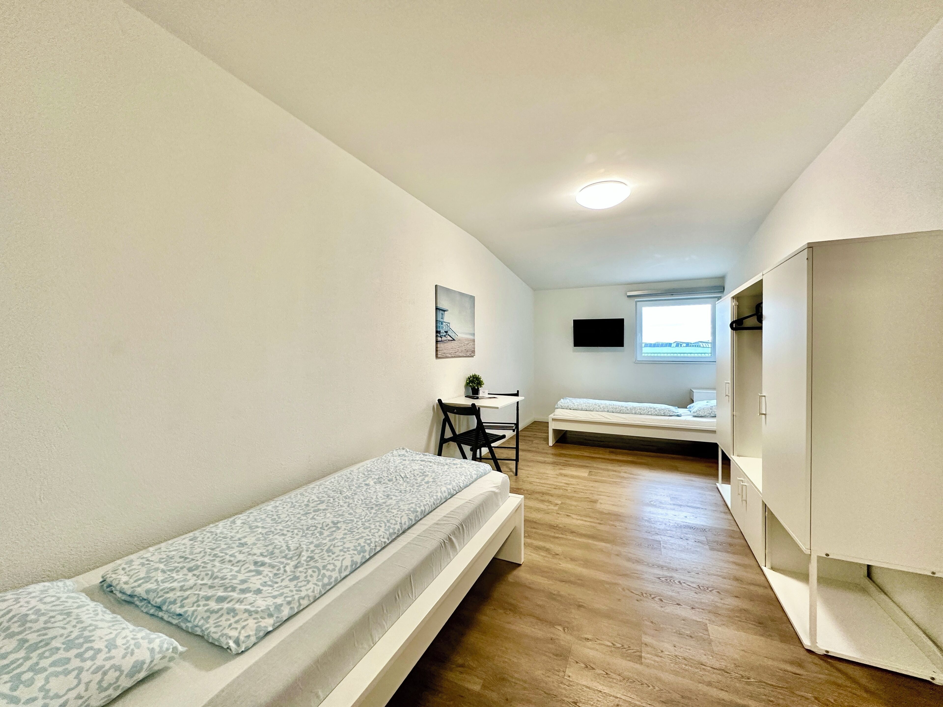 A compact room with two single beds, a desk, a chair, a TV, and a window.