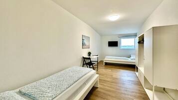 A compact room with two single beds, a desk, a chair, a TV, and a window.